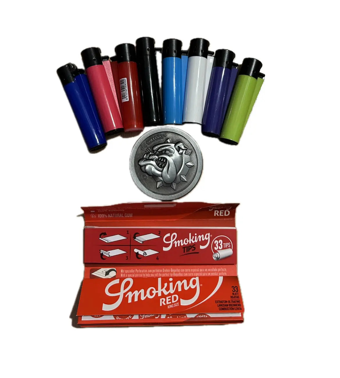 Ein Halbkreis aus bunten rauchigen Clipper-Feuerzeugen aus dem Starterpack Mini thront über einer silbernen Dose mit Drachengravur. Darunter sind die rot-weißen Papierpackungen „Smoking Red“ und „Smoking Tips“ abgebildet. Dazu ein Bulldog Amsterdam Grinder / Gewürzmühle mit verschiedenen Clipper Feuerzeuge 